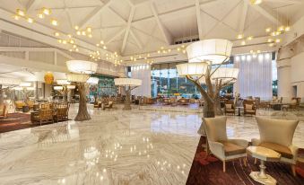 a large , well - lit hotel lobby with marble floors and white walls , as well as several chandeliers hanging from the ceiling at Moon Palace Jamaica