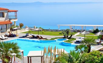 a beautiful outdoor swimming pool area with clear blue water , surrounded by lush greenery and a beautiful view of the ocean at Blue Bay Halkidiki