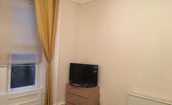 a living room with a television on a stand and a window with yellow curtains at Union Apartments