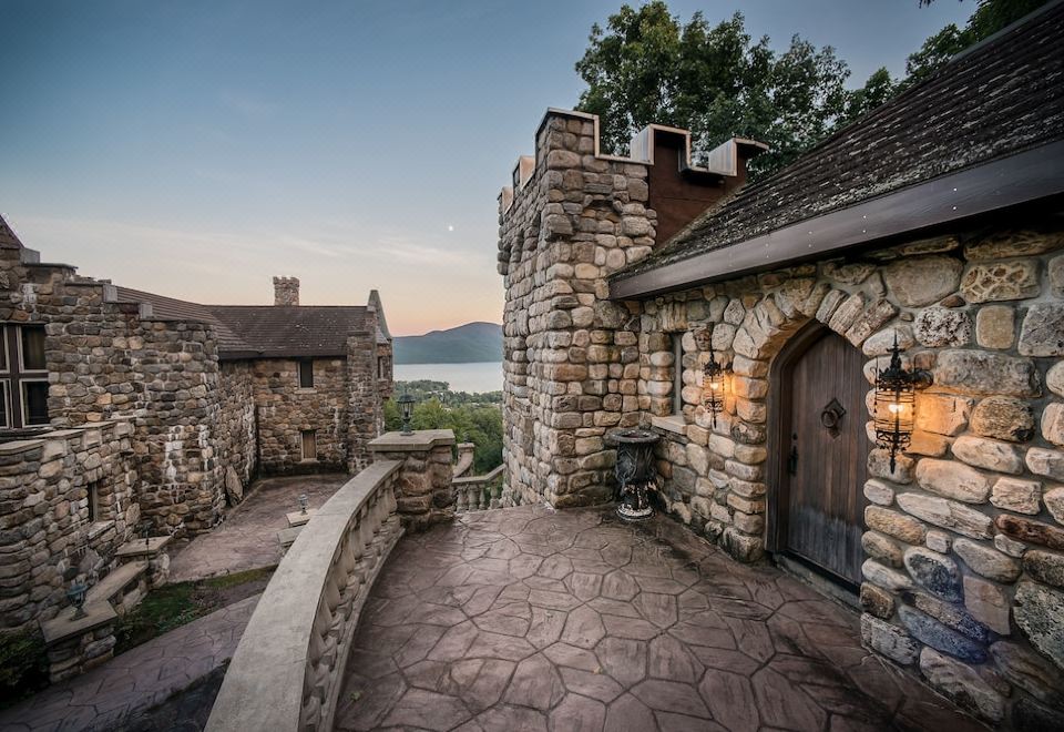 a stone house with a wooden door and a stone walkway leading to it , overlooking a body of water at Highlands Castle Overlooking Lake George Plus 2 Other Castles & Suites