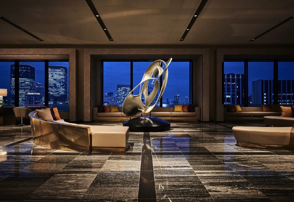 a large , modern living room with a sculpture in the center and floor - to - ceiling windows overlooking a city skyline at The Royal Park Hotel Iconic Osaka Midosuji