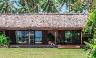 a wooden house with a thatched roof , surrounded by palm trees and a green lawn at The Wakaya Club & Spa