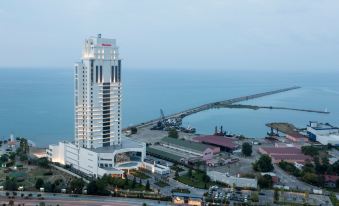 a tall building is situated next to the ocean with a bridge in the background at Sheraton Grand Samsun Hotel