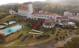 an aerial view of a large white building surrounded by trees , with a swimming pool in front of it at Kawana Hotel