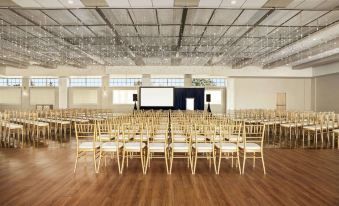 a large room with wooden floors and white walls , filled with rows of gold - colored chairs and a stage at the front at Wyndham Newport Hotel