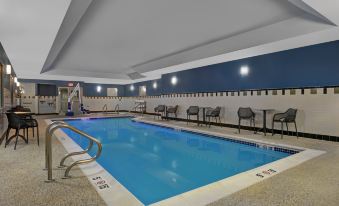 an indoor swimming pool with a diving board , surrounded by lounge chairs and umbrellas , in a well - lit room at Hampton Inn Bath (Brunswick Area)