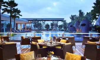a luxurious outdoor dining area with a pool , surrounded by lush greenery and a well - landscaped garden at Hilton Bandung