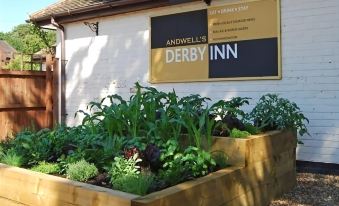 a building with a sign on the side , and several beds of vegetables in front of it at Derby Inn