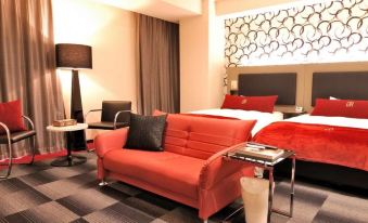 a modern living room with a red couch , black and white checkered rug , and a bed in the background at Green Rich Hotel Kurume