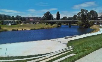 a serene riverside scene with a stone staircase leading down to the water , surrounded by green grass and trees at Crest Motor Inn