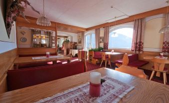 a cozy restaurant with wooden furniture , red curtains , and a view of the mountains outside the window at Hotel Olympia