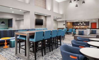 a modern lounge area with blue chairs and tables , a bar , and a large screen tv at Hampton Inn & Suites Bridgeview Chicago