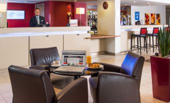 a modern hotel lobby with a reception desk , couches , and chairs , as well as a man sitting behind the counter at Holiday Inn Express East Midlands Airport