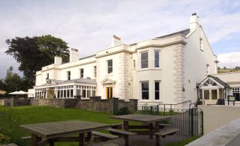 a large white building with a sign on the front and a set of picnic tables in front at Premier Inn Merthyr Tydfil