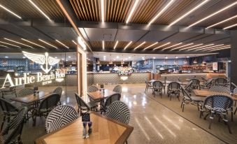 a modern cafe with wooden tables and chairs , a counter , and a sign for the beach bar at Airlie Beach Hotel