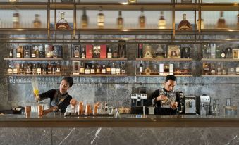 a man and a woman are standing behind a bar , preparing drinks while surrounded by bottles and other items at Royal Ambarrukmo Yogyakarta