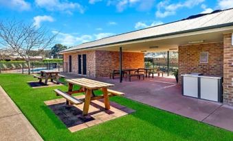 a picnic area with wooden benches , a grill , and a barbecue grill , surrounded by green grass and trees at Potters Apartments