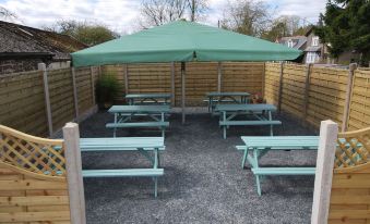 an outdoor area with a green umbrella providing shade for a picnic table and benches at The Punchbowl Hotel