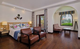 a spacious hotel room with a king - sized bed , two chairs , and a tv . also a potted plant in the room at Holiday Inn Resort Goa