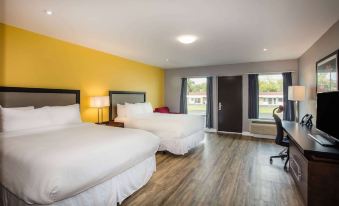 a modern hotel room with two beds , a desk , and large windows , all set against a yellow wall at Ramada by Wyndham Jacksons Point