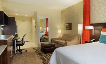 a modern hotel room with a bed , couch , and desk , along with a chair and a window at Home2 Suites by Hilton Merrillville