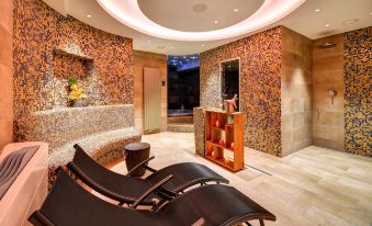 a modern spa room with two reclining chairs , a wooden shelf , and a tiled wall at Hotel Helios