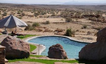 a large outdoor pool surrounded by rocks and grassy areas , with a tent set up nearby at Canyon Lodge