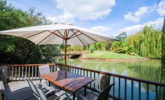 a wooden deck with a table , chairs , and an umbrella overlooks a river surrounded by trees at Perricoota Vines Retreat