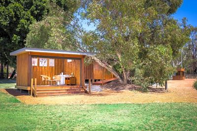 a wooden cabin with a table and chairs set up outside , surrounded by trees and grass at The Swan Valley Retreat