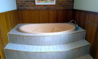 a large bathtub with a silver edge is situated in a room with brick walls at Kerang Motel