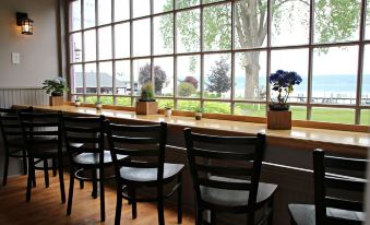 a restaurant with wooden chairs and tables , a large window , and potted plants on the windowsill at Plum Point Lodge