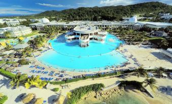 a large swimming pool is surrounded by palm trees and buildings , with people enjoying the beach nearby at Grand Palladium Lady Hamilton Resort & Spa - All Inclusive