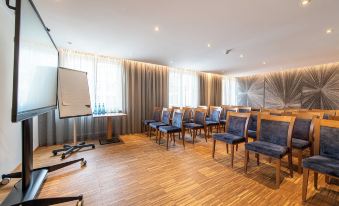 a conference room with wooden flooring , blue chairs arranged in rows , and a whiteboard on the wall at Hotel Post Alpine Cityflair