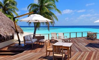 a wooden deck overlooking the ocean , with several chairs and a dining table set up for a tropical vacation at Makunudu Island