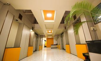 a long , well - lit hallway with yellow and gray walls , white floor tiles , and a palm tree on one side at Hotel Sangam