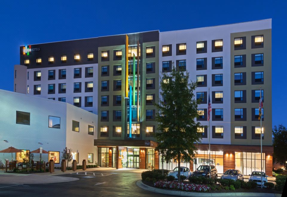 a large , modern hotel building with multiple floors and balconies at night , surrounded by trees and cars parked in the street at Even Hotel Rockville - Washington, DC Area, an IHG Hotel