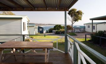 a wooden deck with a table and chairs , overlooking a body of water from a building at NRMA Merimbula Beach Holiday Resort