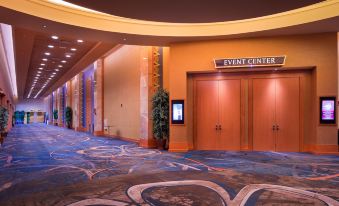 a large , empty event center with blue carpet and wooden doors , along with several potted plants and signage at Seneca Allegany Resort & Casino