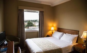 a hotel room with a king - sized bed , a lamp , and a view of the city outside the window at Cairn Hotel