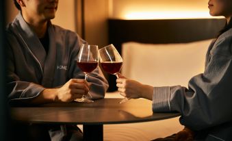 A couple is seated at a table, holding glasses and food, with one of them also holding a wine glass at HOMES Stay Myeongdong