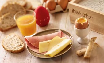 a table with a plate of food , including ham and cheese , next to an egg shell at Ibis Luxembourg Sud