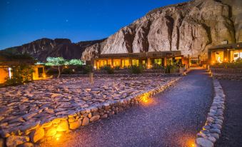 a wooden cabin is lit up at night , surrounded by a stone wall and rock formations at Nayara Alto Atacama