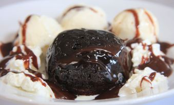 a white plate with four scoops of ice cream , one in the center , surrounded by a bowl of chocolate sauce at Country Roads Motor Inn