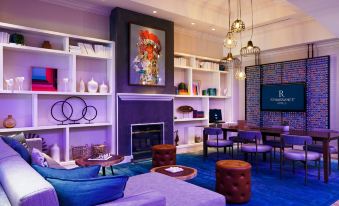 a modern living room with purple and blue furniture , a fireplace , and a large painting at Renaissance Meadowlands Hotel