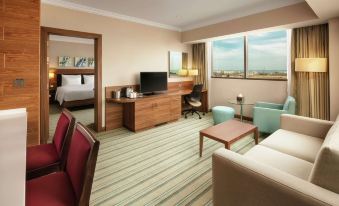 a hotel room with a king - sized bed , a flat - screen tv , a couch , and a dining table at Hilton Garden Inn Al Jubail