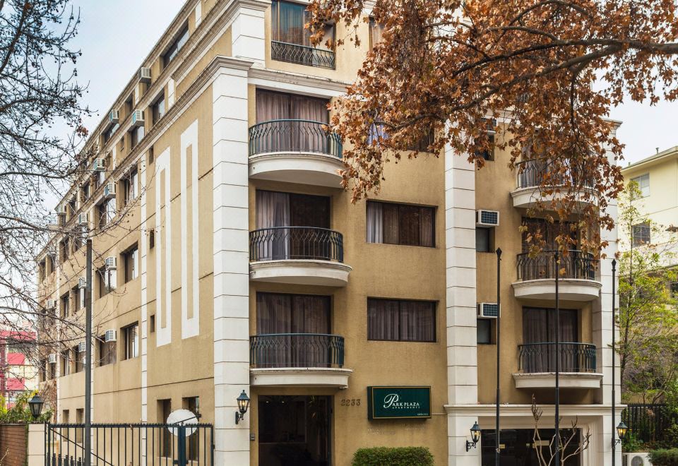 a three - story apartment building with balconies and green signage , situated on a street with trees and other buildings in the background at Park Plaza Apartments