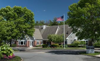 a large building with an american flag on a pole in front of it , surrounded by trees at Residence Inn Boston Westford