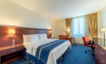 a hotel room with a large bed , blue carpet , and various furnishings such as chairs , tables , and curtains at Hodelpa Garden Court