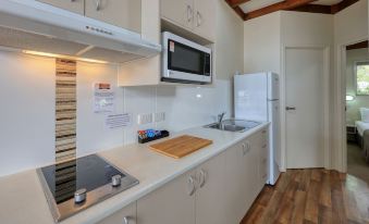 a small , modern kitchen with white cabinets and appliances , including a refrigerator , microwave , and oven at Tasman Holiday Parks - Rollingstone