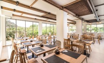a modern , open - air restaurant with wooden tables and chairs , large windows , and a view of trees outside at Matala Bay Hotel & Apartments